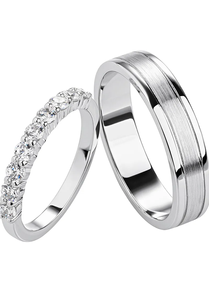 Three silver and rose gold men's wedding bands with diamond accents on a textured surface.