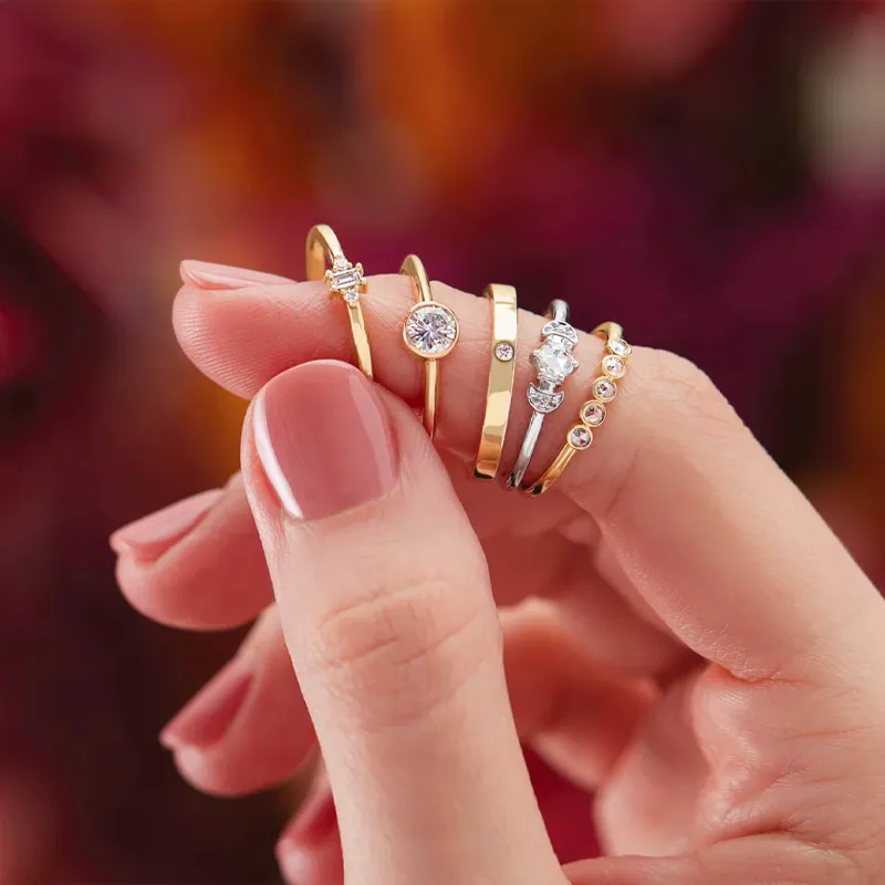 Three elegant gold rings on a pink background, showcasing different styles and designs. Click to explore more at Barthau Jewelle