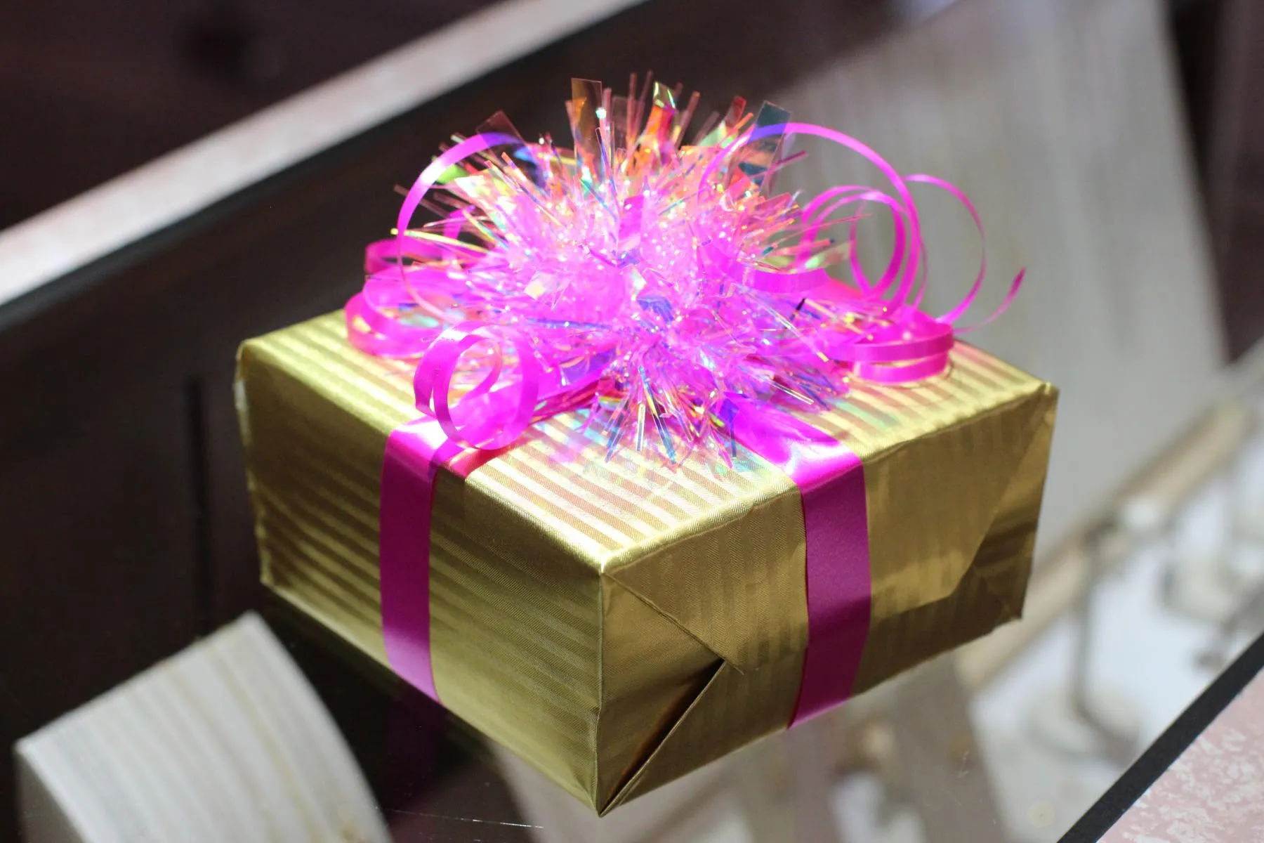 Jewelry gift box wrapped in gold paper with pink ribbon and tinsel