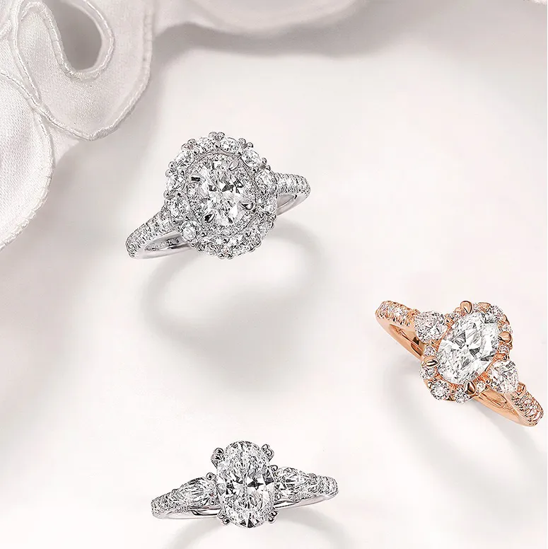 Three elegant engagement rings featuring diamonds, set in white and rose gold, displayed on a soft fabric background. Shop Now.