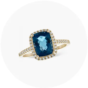Elegant gold ring featuring a large blue gemstone surrounded by smaller diamonds. Click to explore more Fashion Rings.