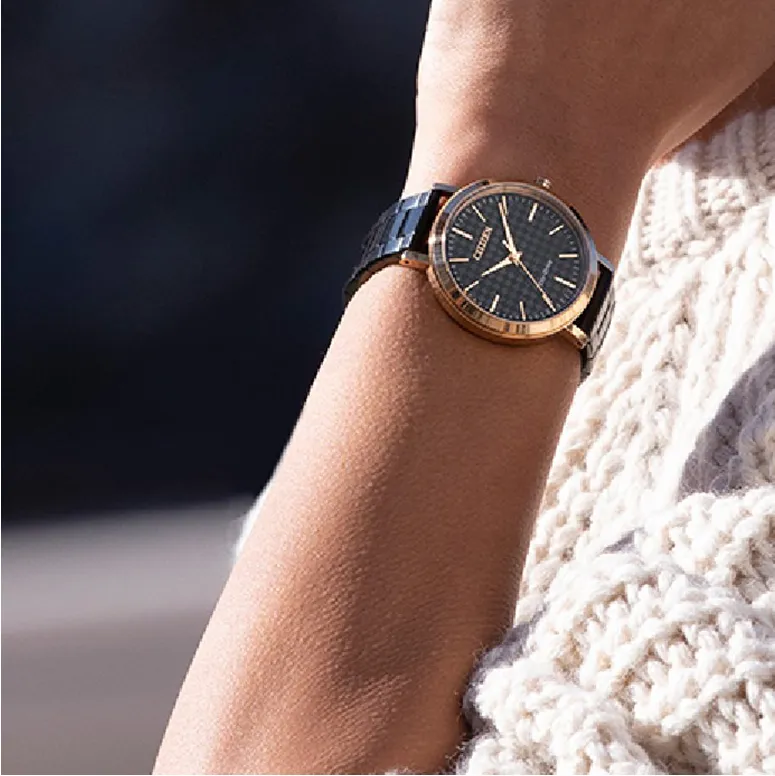 Gold and black watch on a wrist, with a cozy knit sweater in the background. Click to shop timepieces at Mesa Jewelers.