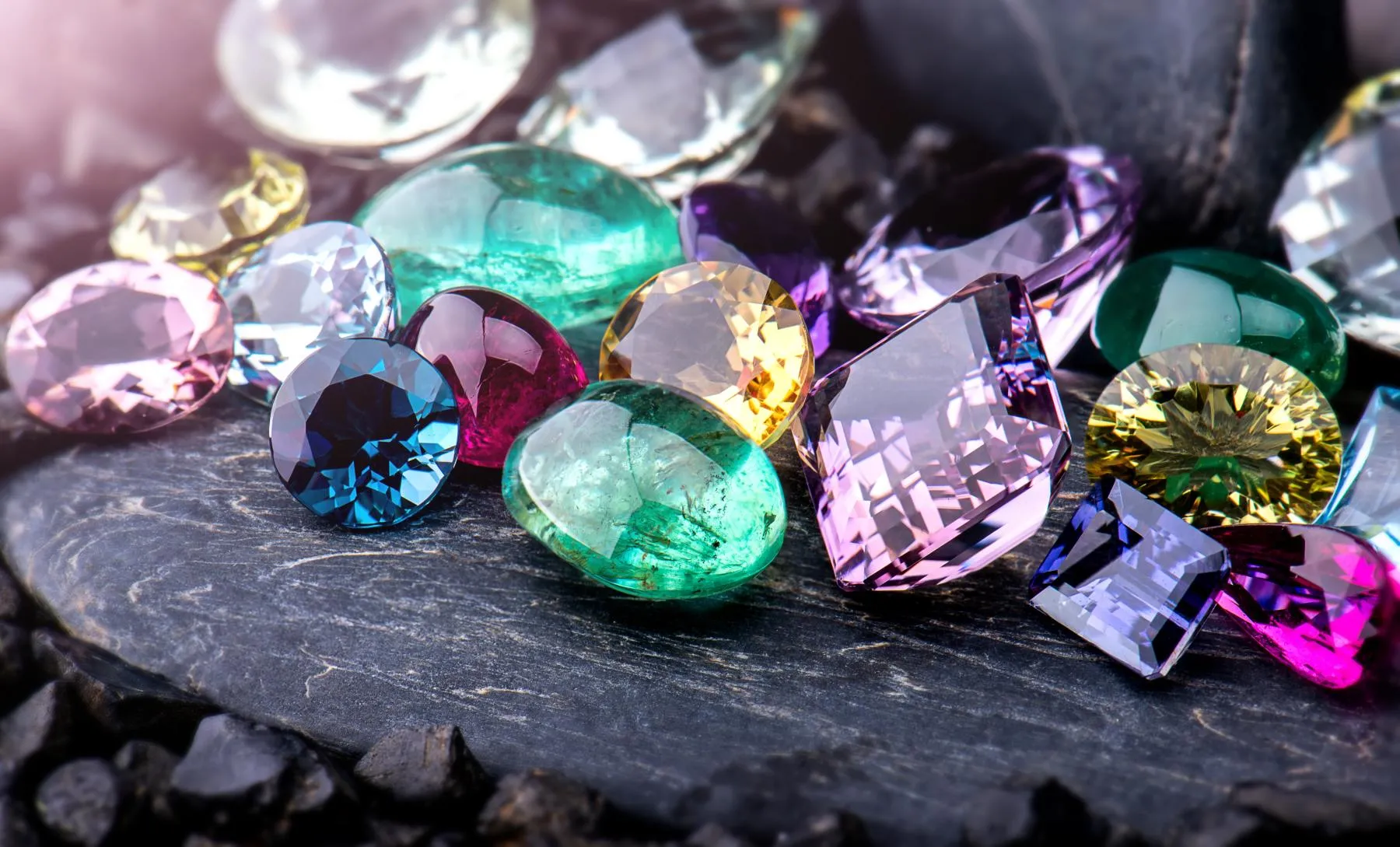 Colorful gemstones scattered on a dark surface. Click to shop now at Monarch Jewelry in Winter Park.